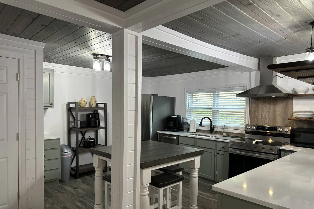 This image captures a bright, functional kitchen space featuring a central island with granite countertops, sleek stainless steel appliances, open shelving for easy access to kitchenware, and an abundance of natural light streaming through a window. The overall impression is of a modern, well-equipped area ideal for both cooking and entertaining.