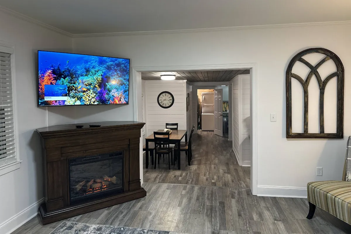 A spacious dining area featuring a dining table, a television displaying a colorful ocean scene, and a cozy fireplace, all set within an inviting, open interior. The table is ready for meals and gatherings, and the atmosphere suggests warmth and togetherness, tying in the adjacent spaces to the kitchen.