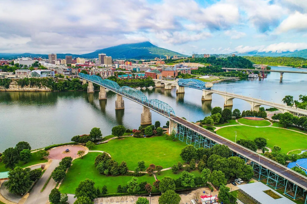A wide view of a river bordered by a bridge, the city skyline, and distant mountains. The scene is tranquil, showcasing both natural beauty and easy access to urban activities, with gentle water reflecting the city lights.