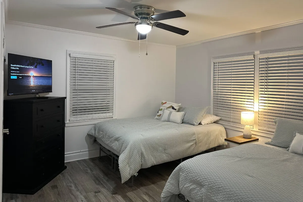 A cozy bedroom with two beds, a television, and a nightstand with a lamp. Soft lighting and textiles create a welcoming space perfect for unwinding and enjoying a movie before bed.